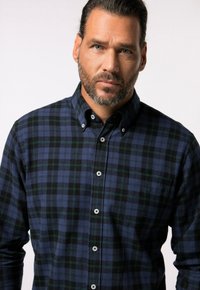 Camicia button-up con motivo a quadri nei colori navy, nero e verde. Materiale in cotone con una texture morbida e bottoni bianchi.