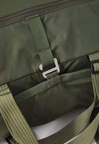Sac à dos en nylon vert olive avec des bretelles en toile, quincaillerie argentée et fermeture éclair. Présente des coutures renforcées et une surface texturée.
