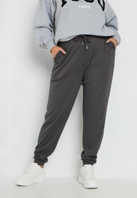 Grijze geribbelde joggingsbroek met een elastische tailleband en zijzakken, gecombineerd met een grijze sweatshirt met zwarte letters. Witte sneakers.