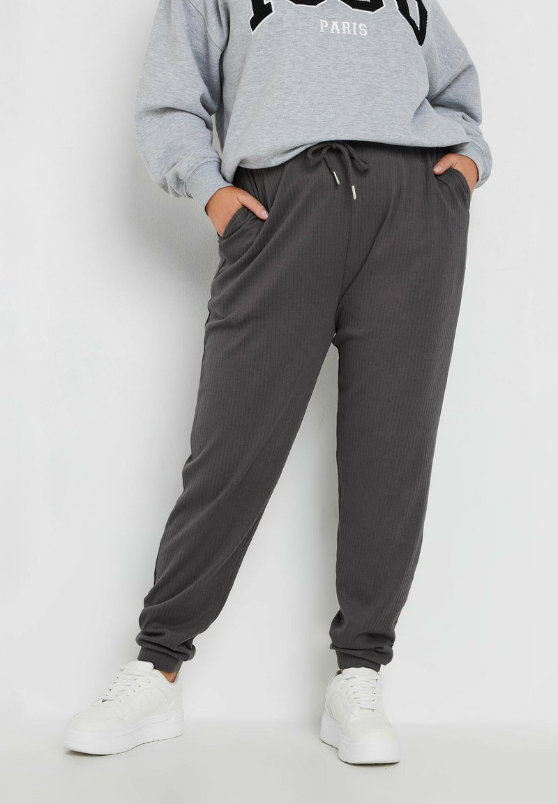 Grijze geribbelde joggingsbroek met een elastische tailleband en zijzakken, gecombineerd met een grijze sweatshirt met zwarte letters. Witte sneakers.