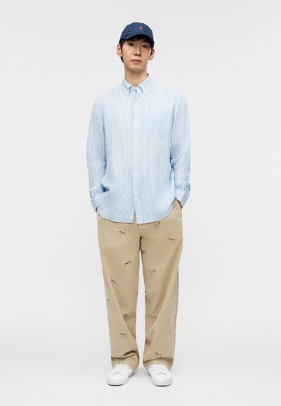 Light blue, striped button-up shirt with chest pocket; beige pants with small dog embroidery; navy cap; white sneakers.