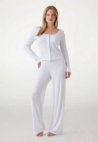 Top blanco de manga larga con detalles de botones y pantalones blancos de corte holgado, ambos hechos de tela suave. Textura sencilla y lisa en toda la prenda.