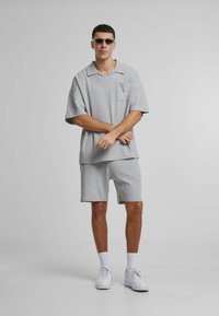 Polo gri din tricot cu mânecă scurtă și buzunar pe piept, asociat cu pantaloni scurți asortați. Adidași albi și ochelari de soare completează ținuta.
