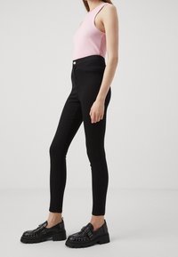 Svarta smala jeans kombinerade med en ljusrosa ribbad linne och svarta nitar loafers. Klädseln har en figurnära silhuett och en stilren design.