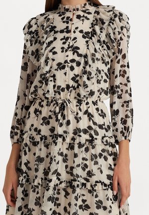 Biała sukienka z czarnym kwiatowym wzorem, długie bufiaste rękawy, falbany na piersi i warstwy spódnicy oraz taliowany pas z wiązaniem.