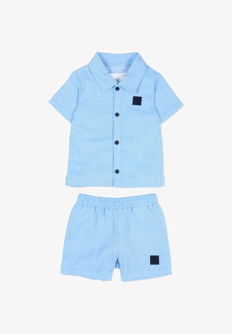 Chemise bleu clair pour tout-petit avec col et boutons, associée à un short à taille élastique assorti, les deux ornés de petits patches carrés foncés.