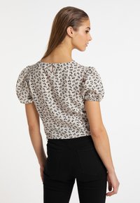 Kortærmet bluse i creme med et sort blomsterprint, med puffede ærmer og detaljer med nøglehul på ryggen. Sammen med sorte bukser.