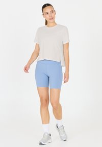 Ljusgrå croppad t-shirt med korta ärmar i kombination med blå högmidjade shorts med sidofickor. Modellen bär silverfärgade sneakers.