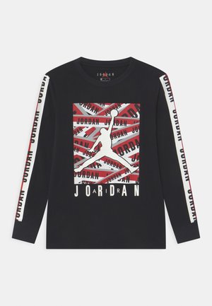 Czarna koszula z długim rękawem z białym i czerwonym napisem „Jordan” na rękawach oraz dużym konturem Jumpman z powtarzającym się napisem „Jordan” na piersi.