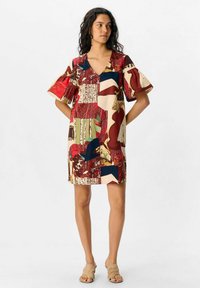 Robe à manches courtes avec un design en patchwork dans des tons rouges, beiges et bleus. Encolure en V et coupe décontractée avec des motifs de texture variés.