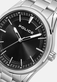 Reloj de acero inoxidable plateado con un dial negro texturizado, marcadores de hora plateados y logotipo. Cuenta con un bisel pulido y una pantalla de fecha.