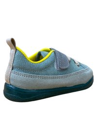 Zapato de tela azul claro con detalles en gamuza gris, suela de goma verde, forro amarillo y correa de velcro. Lengüeta trasera para facilitar el uso.