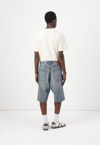 Light beige t-shirt, loose-fitting, paired with knee-length blue denim shorts. Sneakers with black accents, white socks. Minimalist design.
