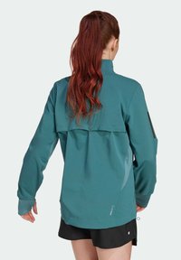 Teal windbreaker with a high collar, long sleeves, and a flap pocket. Features a lightweight material and elastic cuffs for a snug fit.