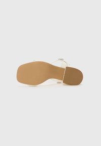 White heeled sandal with a smooth upper and a tan rubber sole. Features a secure ankle strap and a block heel with a textured surface.