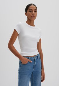 T-shirt bianco a maniche corte con scollatura rotonda, abbinato a jeans di denim blu. Il tessuto sembra morbido e aderente alla vita.