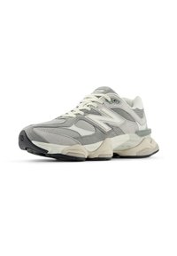 Sive in bele teka New Balance teka za tek z mrežastim in antilopnim zgornjim delom, robustnim podplatom in logotipom "N" na strani, pod kotom, da prikaže sprednji in zunanji del.