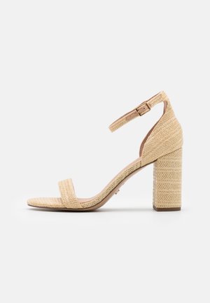 Sandale à talon bloc tressé beige avec bride à la cheville et boucle, bout ouvert, et surface texturée sur le talon et les brides.