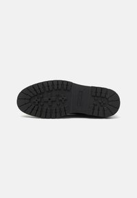 Suela de zapato de goma negra con profundas marcas y surcos. Presenta un diseño plano y estrías para una mejor tracción. Marcado visible.