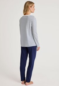 Gestreepte lange mouw top in wit en marine, gecombineerd met effen marinebroeken. Zachte stof, relaxte pasvorm en recht gesneden ontwerp.