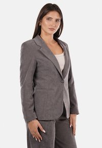 Blazer grigio in tessuto morbido con revers a punta, chiusura con un bottone e due tasche frontali. Vestibilità slim con una consistenza liscia.