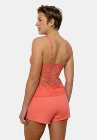 Débardeur en dentelle corail avec bretelles réglables, présentant un design texturé et un short plissé assorti avec un ourlet en feston.