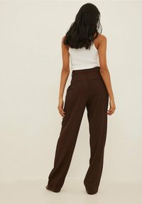 Bruna högmidjade byxor med vida ben, som har sidofickor och en slät textur. Bakifrån visar de minimalt med detaljer.