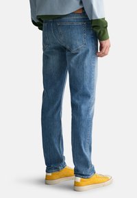 Lichtblauwe spijkerbroek met rechte pijpen, voorzien van achterzakken en subtiele vervaging. Gecombineerd met gele sneakers en een tweekleurig shirt.