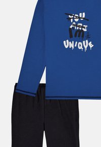 Long-sleeve blue top with white and black text design, paired with black pants. Features a round neckline and elastic waistband.