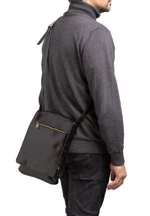 Man die een donkergrijze coltrui en zwarte jeans draagt met een zwarte leren schoudertas met een ritsvak aan de voorkant.