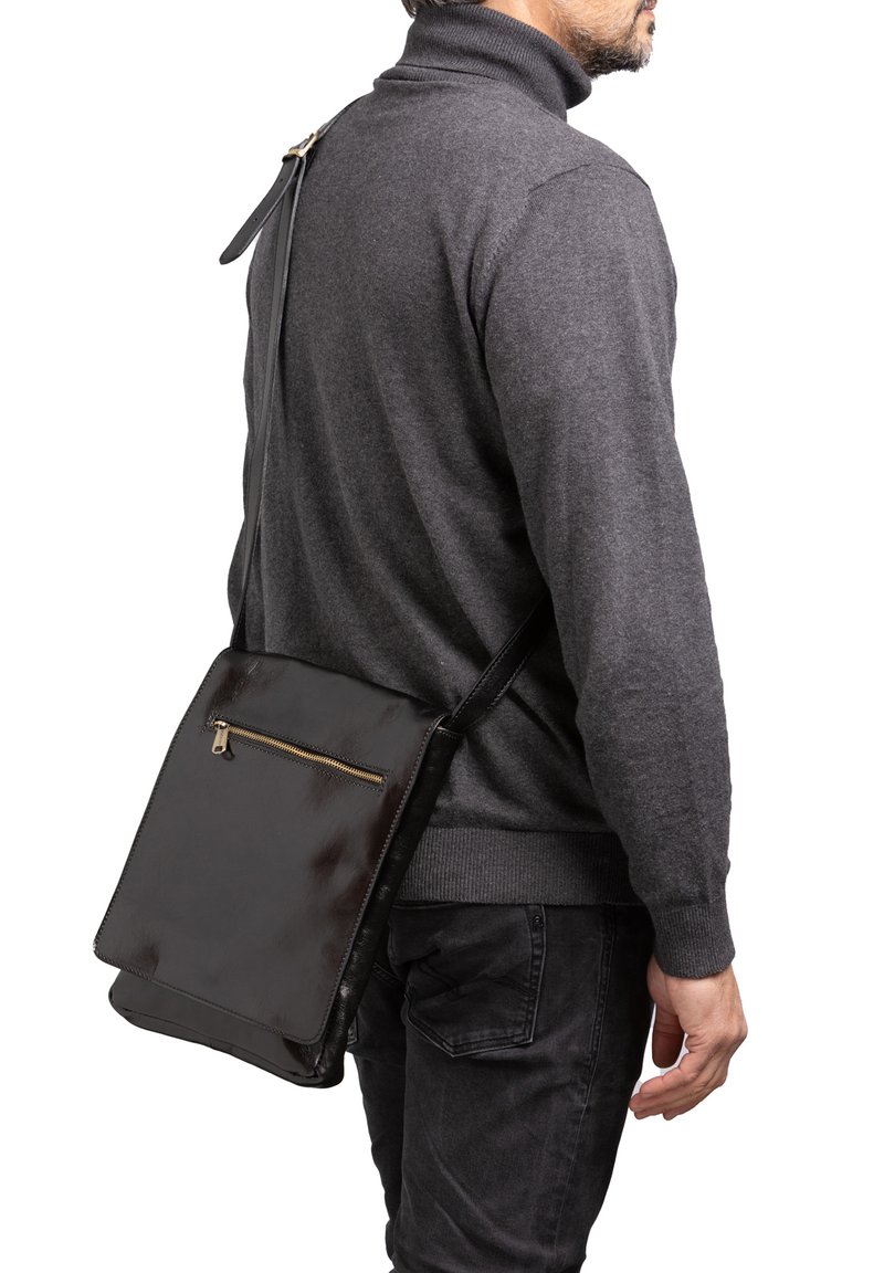 Mann trägt einen dunkelgrauen Rollkragenpullover und schwarze Jeans sowie eine schwarze Leder-Umhängetasche mit einer vorderen Reißverschlusstasche.