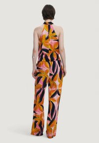 Tuta floreale con design a collo halter. Presenta bold motivi arancioni, rosa e neri, con gambe ampie e una texture di tessuto morbida.