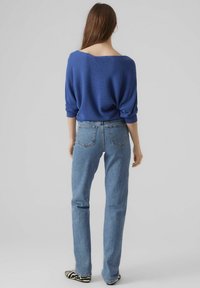 Pull bleu côtelé avec un large décolleté, associé à un jean droit bleu clair. Des chaussures rayées complètent la tenue.