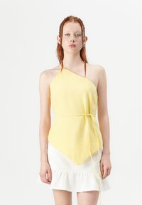 Yellow, asymmetrical halter top with a textured finish, tied at the waist. Paired with a white ruffled skirt, creating a layered look.