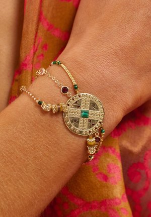 Gold bracelet featuring a circular pendant with intricate patterns, a green stone, and various beads, including red and green accents.