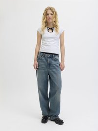 White fitted t-shirt with a black bow detail at the neckline, paired with light blue baggy jeans and black chunky shoes.