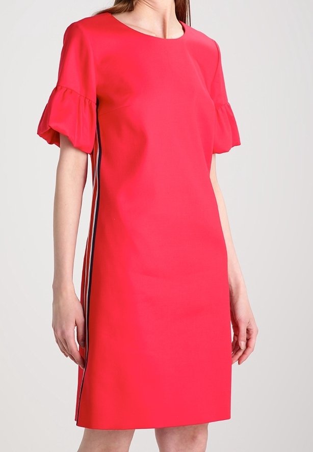 Femme portant une robe rouge vif mi-longue avec des manches courtes à volants et des rayures noires et blanches sur les côtés.