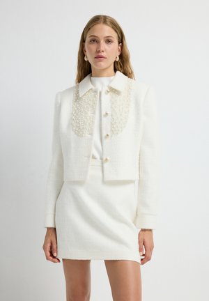 Kürzeste weiße Bouclé-Jacke mit einem kragen, der mit Perlen verziert ist, mit einer Knopfleiste vorne und strukturierten Schultern, kombiniert mit einem passenden Rock.