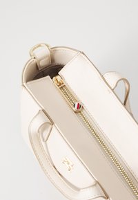 Borsa a mano in pelle beige con chiusura superiore a zip, hardware dorato e foderatura interna. Presenta due manici corti e un dettaglio con logo.