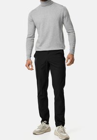 Maglione grigio a collo alto, pantaloni neri aderenti e sneakers beige. Tessuto morbido, design attillato e pantaloni alla caviglia dallo stile minimalista.