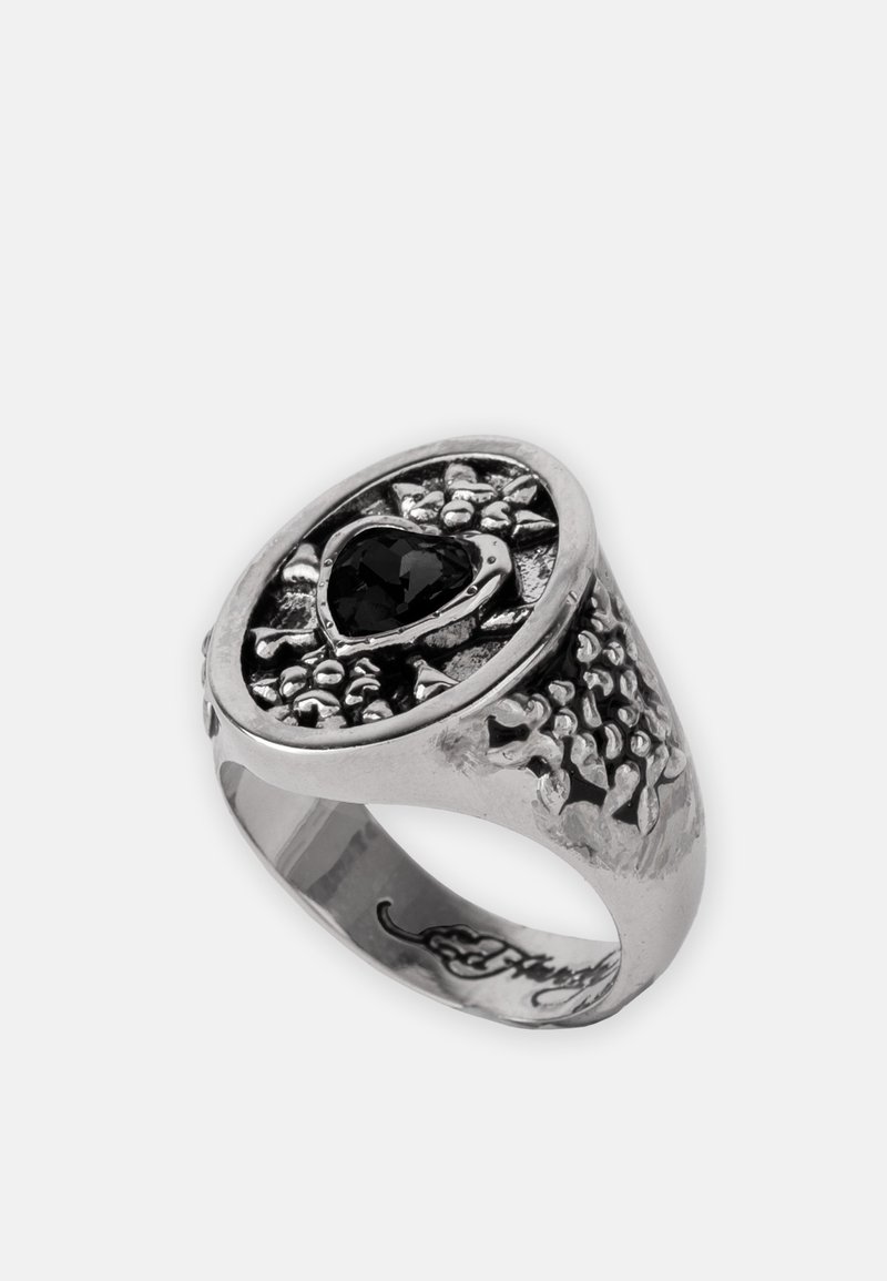 Zilveren ring met een gestructureerd oppervlak, met een hartvormige zwarte edelsteen in het midden en decoratieve bloemaccenten eromheen.