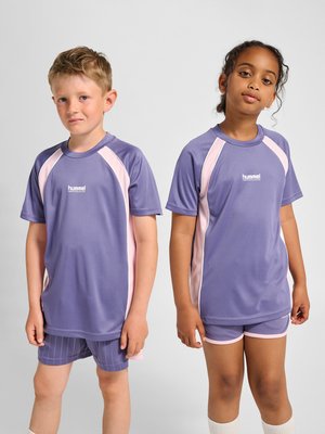 Dwoje dzieci stoi obok siebie, ubrane w pasujące fioletowo-różowe ubrania sportowe z logo hummel na jednolitym szarym tle.