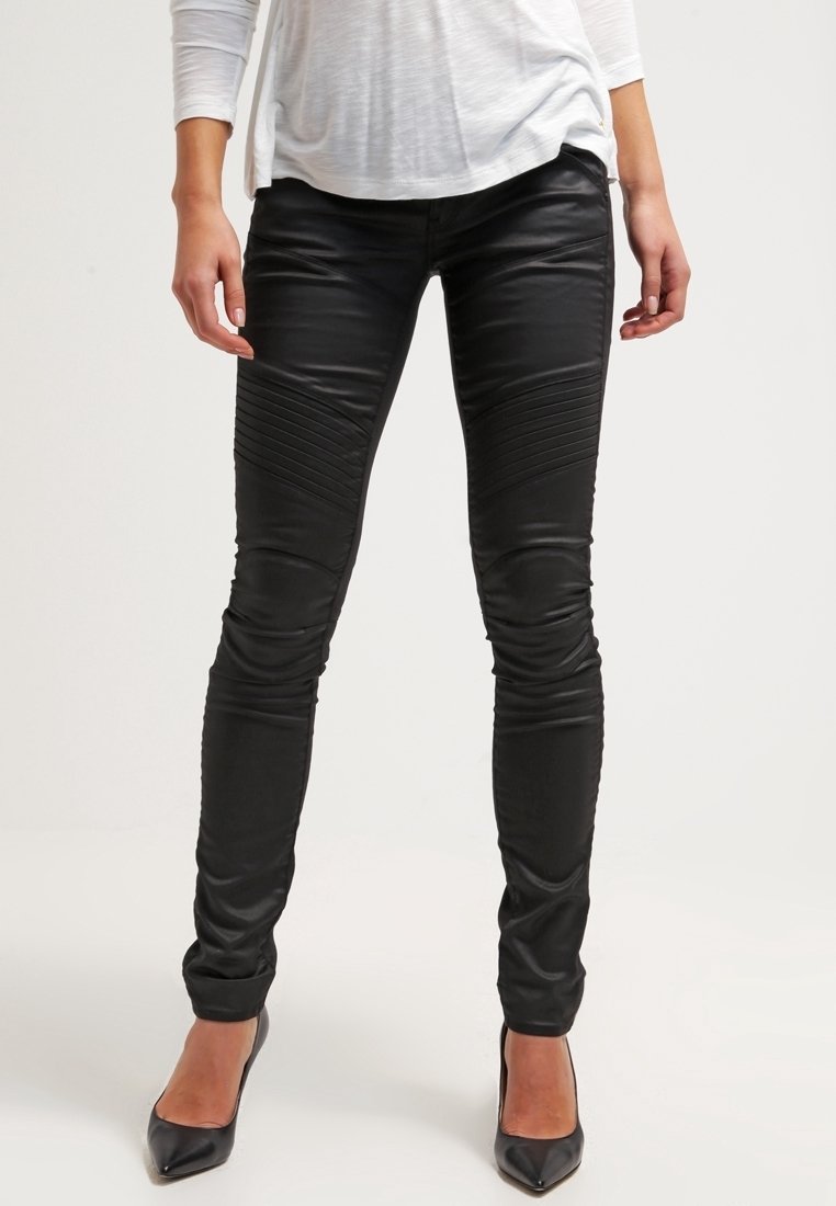 Pantalones ajustados de cuero sintético negro con detalles acanalados en los muslos y acabado elegante, combinados con zapatos de tacón alto negros.