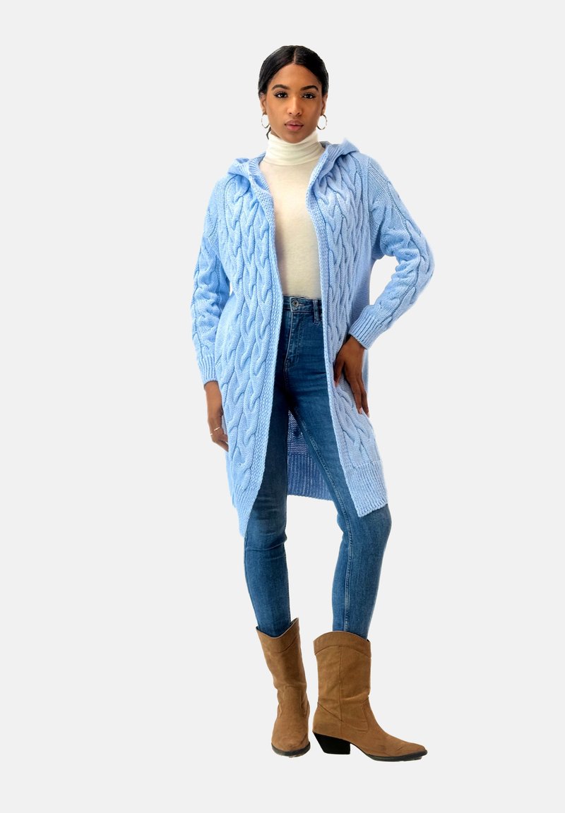 Ljusblå kabelstickad cardigan med huva, öppen fram, texturerade ärmar, i kombination med ljusa denimjeans och bruna ankelboots.