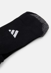 Schwarze Sportsocke mit geripptem Muster, grauen Akzenten an Ferse und Zehen sowie einem weißen Logo mit drei parallelen Streifen.