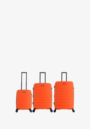 Three bright orange hard-shell suitcases of small, medium, and large size with extended black handles and four spinner wheels each.