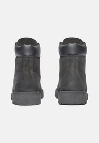 Botines negros de tobillo fabricados con materiales de ante y cuero, que presentan un cuello acolchado, parte superior texturizada y una suela de goma con relieve para mayor agarre.