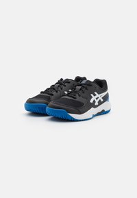 Baskets de sport noires avec une tige en mesh, accents blancs et bleus, semelle texturée et lacets noirs. Présente un logo distinctif sur le côté.
