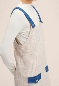 Robe légèrement texturée avec un motif tissé pastel, bretelles en denim bleu et deux poches avant boutonnées.