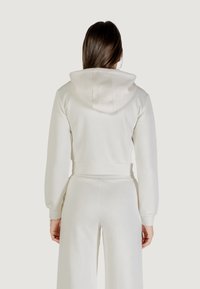 Felpa bianca accorciata, tessuto texturizzato con un motivo sottile, dotata di cappuccio e polsini a coste, abbinata a pantaloni a gamba larga coordinati.